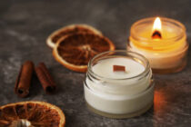 Handmade burning candle with wooden wick in white glass jar with cinnamon and dry oranges at the background, winter cozy home decoration